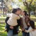 A joyful family sharing a tender moment in a sunny park setting.